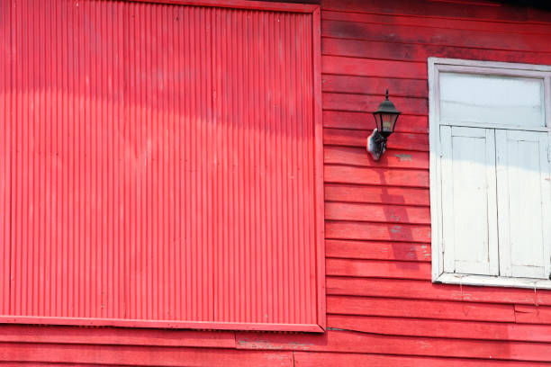 A vibrant red wooden building featuring vertical planks and a simple white window contrasts beautifully against the clear daylight, showcasing unique architectural details.