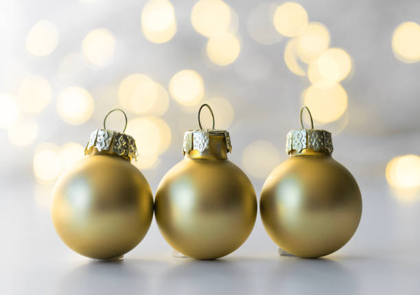 Close-up of golden Christmas baubles scattered against a sparkling bokeh background. The soft focus on the lights creates a warm, festive atmosphere, perfect for holiday-themed projects, greeting cards, and Christmas decorations.