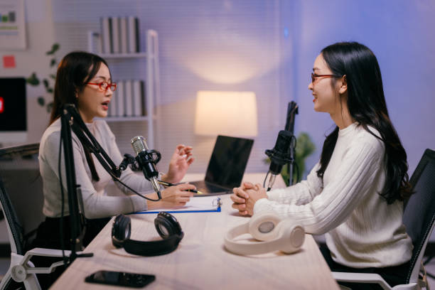 istock Two young female podcasters are recording an interview in a professional studio, using microphones and headphones, with a laptop and notes on the table 2185219013