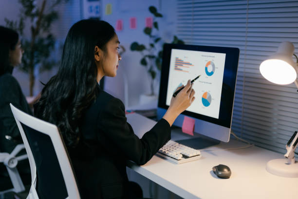 istock Focused young businesswoman analyzing data and pointing at charts on computer screen late at night in office, showcasing ambition and dedication to career 2185219568