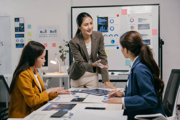 Three asian businesswomen are discussing charts and analyzing statistics during a meeting in a modern office, collaborating on important business decisions Three asian businesswomen are discussing charts and analyzing statistics during a meeting in a modern office, collaborating on important business decisions digital marketing stock pictures, royalty-free photos & images