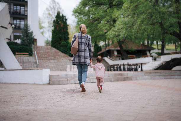 A mother holding hands with her young daughter as they walk through a picturesque outdoor setting. The scene captures the bond between parent and child, perfect for themes of family, nature, and togetherness.