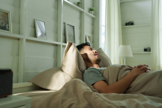 istock Asian man sleeping peacefully in bed with beige bedding with morning light, relaxation and calmness. 2185221025