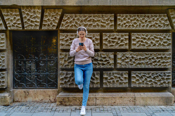 istock Young woman uses phone while leaning against wall in city 2185222259