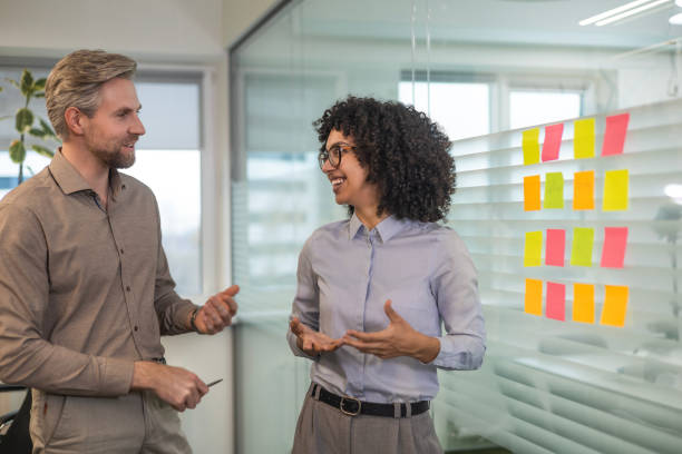 istock Two business people discussing work together using sticky notes on glass wall in a modern office 2185223635