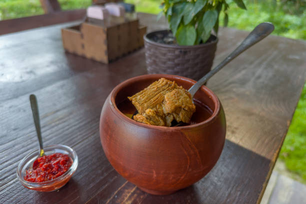 Thick soup-stew bograch served in clay pot with chili sauce Eros Pista on a wooden table outdoors