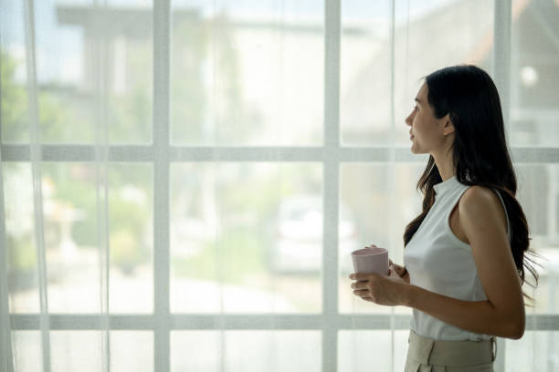 istock A woman is holding a cup and looking out the window 2185228331