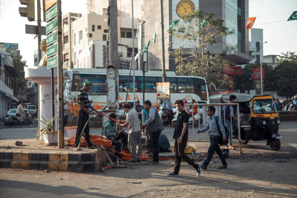 Nagpur Area, India - A group of workers is engaged in street maintenance activities at a busy urban intersection, while pedestrians and vehicles navigate around them during daylight hours.