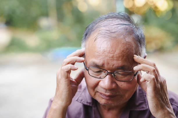 istock senior man is experiencing stress or discomfort, holding his head with both hands. His expression reflects moment of contemplation or worry, set against blurred natural background 2185249054