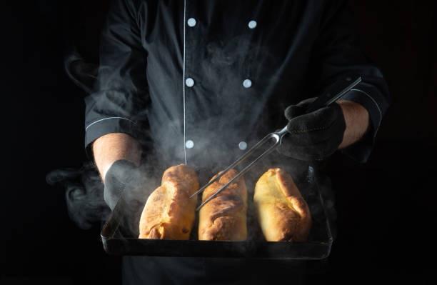 istock A skilled chef in a black uniform carefully presents three golden-brown bread rolls, steaming and fresh from the oven, amidst a dark kitchen setting filled with anticipation 2185251942