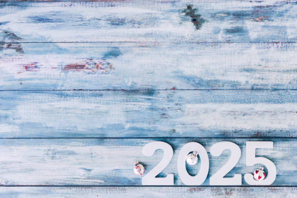 Flat lay of 2025 numbers in white adorned with three small Christmas baubles set against a light blue vintage background. A design perfect for modern Christmas and New Year cards for children.Color editing. Part of a series.