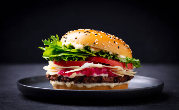 istock Burger with beef, cheese, vegetables on black plate. Dark Background. Close up. 2185257467