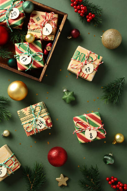 istock Christmas flat lay composition with wrapped gifts numbered for an advent calendar, surrounded by Xmas ornaments, pine branches, and berries on a green background 2185258083