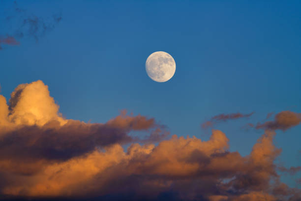 Full Moon in Colorful Sunset Sky - Large warm-toned moon in sky with alpenglow lighting up clouds above mountains.