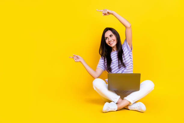 istock Photo of cheerful positive lady sit two arm index empty space interested look modern technology sale isolated on yellow color background 2185266302