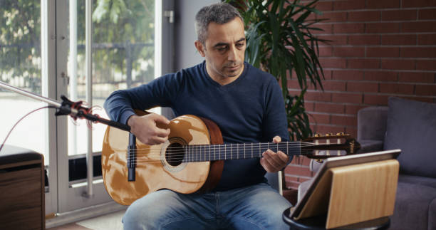 istock Man playing guitar reading notes online on digital tablet and recording sound 2185272379