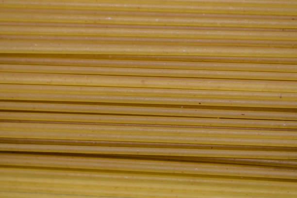 Long spaghetti. Spaghetti background. Yellow long spaghetti on black background. Thin macaroni arranged in rows. Yellow Italian pasta. Raw spaghetti wallpaper. Thin spaghetti. Food concept.