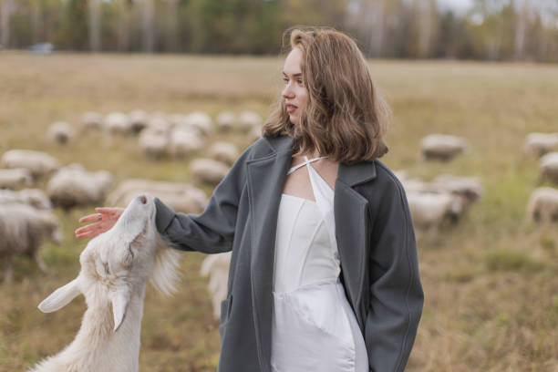 Blonde woman in coat in field with sheep
