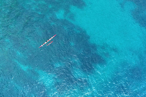 Top aerial view of a classic wooden Hawaiian Outrigger Canoe Boat, just outside the Kamakahonu Beach on a sunny day, Kailua Kona, Hawaii