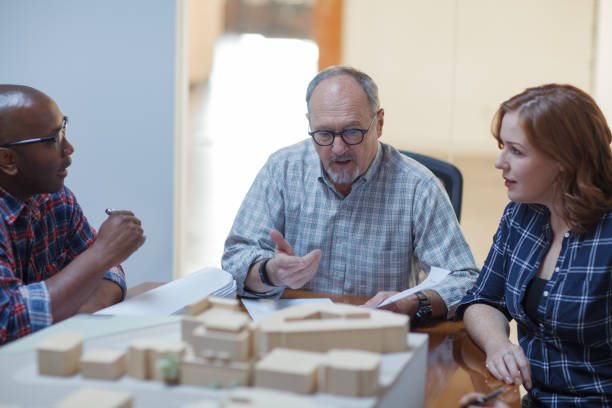 istock Senior man designer discusses architectural model plan with multiracial colleagues teamwork group meeting in design urban planning office 2185285018