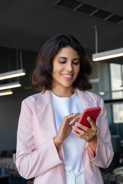 istock Young Indian woman manager using cell phone mobile app for call, business communication, trading. Latin Hispanic female businesswoman holding smartphone for online work, standing in office. Vertical 2185287825