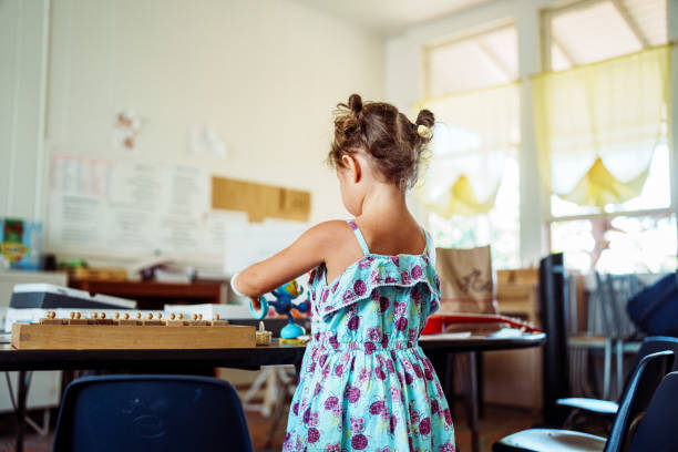 Rear view of a preschool Eurasian girl wearing a dress and playing with toys in a classroom while attending a religious program at her family's Christian church.