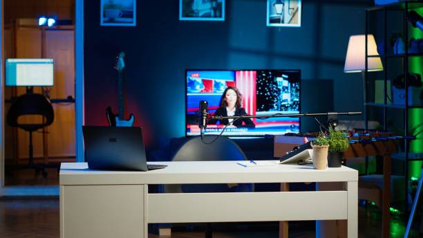 istock Notebook device sitting on table, news broadcast running on TV in background 2185295035
