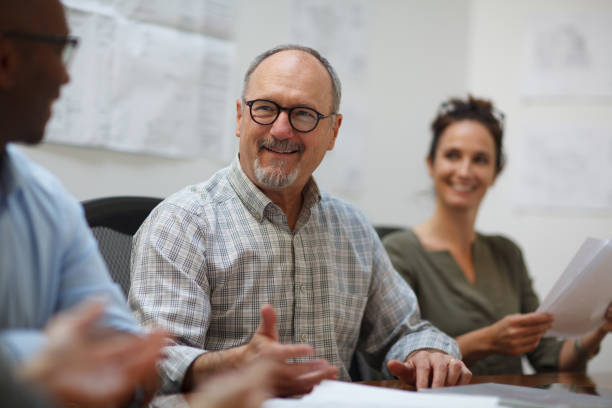 istock Senior man talks smiling in meeting with work colleagues while sitting at table in design office 2185295855