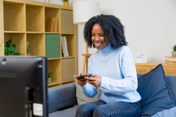 istock Young woman sitting on couch playing videogames with controller 2185297354