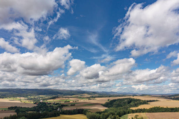An aerial view of Sarny's picturesque fields and forests under a vast sky filled with dynamic clouds, capturing the tranquility and openness of Lower Silesia’s rural landscape.