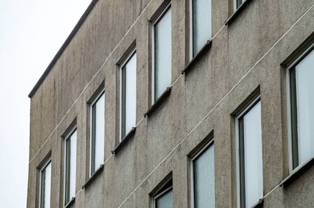 Low angle view of grey concrete facade of modernist building showing multiple windows and white lines