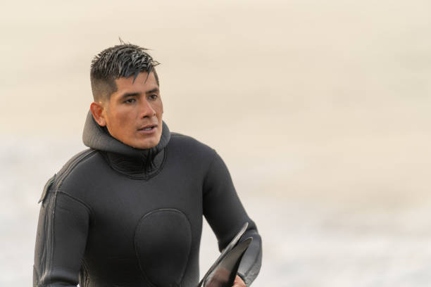 Latin young fisherman in a wetsuit with a cold expression coming out of the water