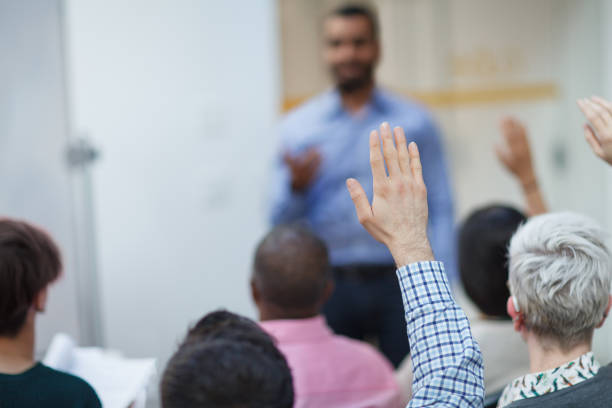 Man hand raised in class lecture training seminar in education school classroom asking question to teacher