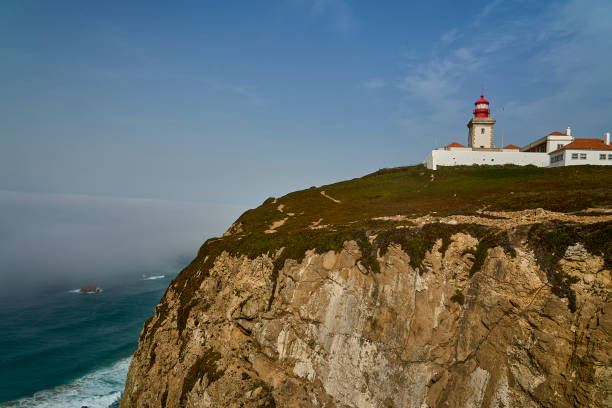 waves breaking at the lighthouse of at the rugged rocky coastline at cabo da roca, the western most point of european mainland, along the atlantic ocean of Portugal with steep cliffs and blue water.