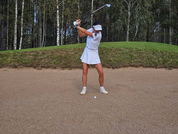 istock Woman practicing golf swing in a sand trap surrounded by trees at a golf course 2185330087