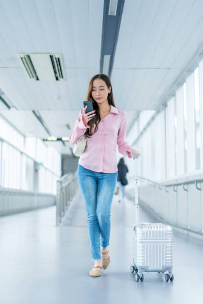 istock Asian Woman with Luggage Using Phone Walking Through Covered Pedestrian Walkway 2185331265