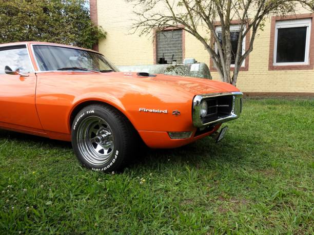 Speyer, Germany – September 15, 2024: An orange Pontiac firebird 1968 parked on green grass by a brick building