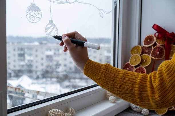 istock Creative enthusiastic unrecognizable woman in sweater paint window with white marker. Advent candle decoration on big clear window. Snowy winter outside 2185337981