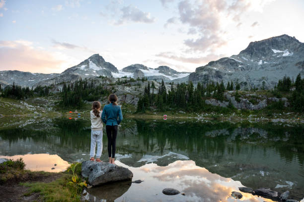 Sisters stand on lakeshore at sunset