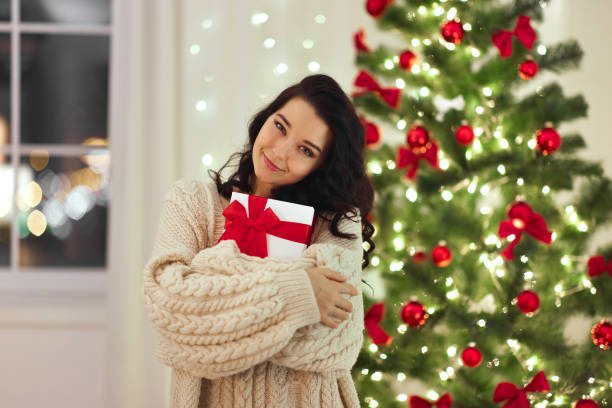 istock Woman Embracing Christmas Gift with Joyful Smile by Festive Tree 2185339157