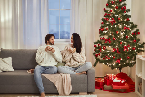 Couple Enjoying Hot Drinks Together by a Christmas Tree at Home