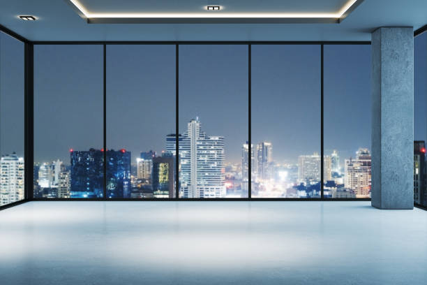 istock Empty modern room with large windows overlooking a city skyline at night. Minimalist interior design with exposed concrete walls. 3D Rendering 2185341087
