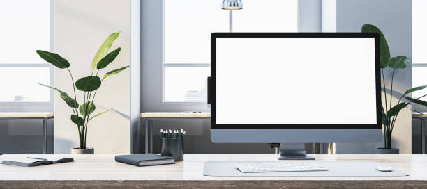 istock Desktop computer with blank screen on an office desk, with plants and large windows in the background. 3D Rendering 2185341223