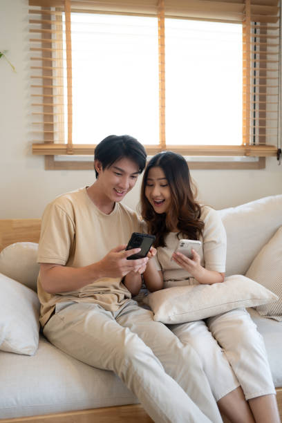 istock Relaxed asian couple laughing at shared content on smartphones 2185343929
