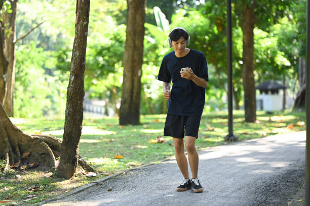 istock Young man holding mobile phone jogging along a paved path in a park on a sunny day 2185344005