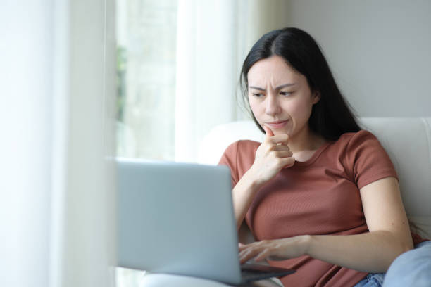 Suspicious asian woman checking laptop content at home stock photo