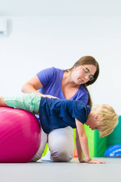 istock Young boy with female physical therapist exercising using ball during therapy session. Child physical therapy. Bilateral coordination. 2185348890