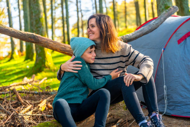 Mother embracing her son sitting next to camping tent