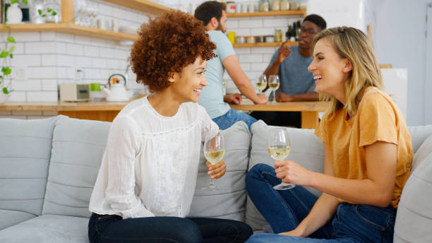 istock Two Couples Relaxing On Sofa At Home With Glass Of Wine Talking Together 2185355419