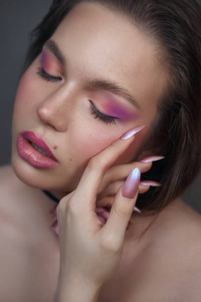 istock model is gently touching her face, highlighting her soft pink eyeshadow and glossy lips. Her long, manicured nails add an elegant touch, conveying confidence and beauty in a calm environment 2185355452